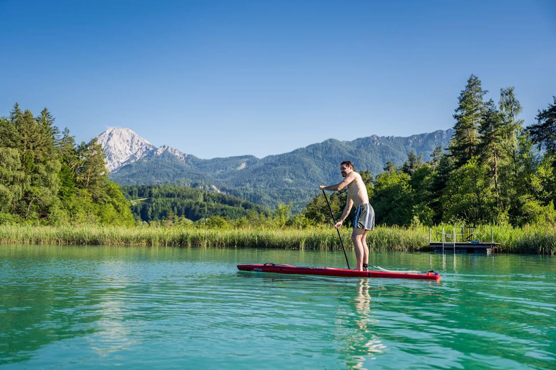 Stand-up Paddle auf spiegelglattem Alpensee im goldenen Abendlicht